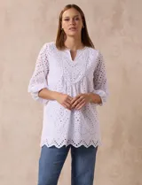 Blusa blanca de algodón con bordado broderie, cuello a la base con escote en V y mangas tres cuartos amplias con puño elastizado.