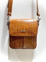 Bandolera marrón con textura simil cuero de cocodrilo, correa larga regulable y logo metálico plateado en el frente.