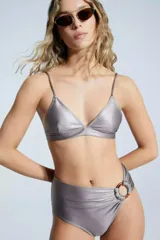 Corpiño de bikini plateado, de corte triangular fijo con elástico inferior de 2 cm. Breteles regulables y espalda con ganchito. Detalle de pinzas en las tazas, con espacio para colocar almohadillas de relleno.
