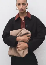 Chaqueta corta de color negro, con cuello camisero, cierre frontal de botones y bolsillos de parche.