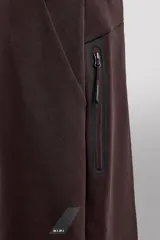 Pantalón jogger color marrón oscuro, corte regular fit, confeccionado en tejido técnico compacto de algodón con elasticidad. Cuenta con cintura elástica ajustable con cordón, bolsillos frontales y bolsillo lateral con cierre de cremallera.