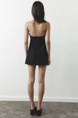 Vestido corto negro sin mangas, con escote palabra de honor y pespuntes marcados. Cierre trasero con cremallera oculta.