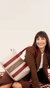 Cartera color crema con franjas horizontales marrón y rojo. Tiene correa corta y correa larga ajustable, división al medio, bolsillo trasero y bolsillos internos.