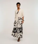 Pollera larga (midi) de corte evasé, con cintura elástica y lazo. Presenta un estampado grande en blanco y negro de motivos tropicales como hojas de palmera y flores.