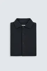 Camisa color beige de corte slim fit, confeccionada en tejido elástico que minimiza las arrugas. Tiene cuello italiano abierto, manga larga con puños abotonados y cierre frontal con botones.