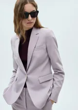 Blazer color beige con solapas de muesca, cierre frontal con un botón, hombros estructurados, corte entallado, forro interior y dos bolsillos de ribete en la parte delantera.