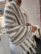 Chal tejido a mano en lana merino color crudo con rayas marrones y flecos en los extremos. Presenta etiqueta de cuero grabada con el logo de la marca.