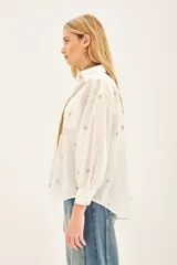 Camisa blanca de algodón con bordado de corazones dorados, corte amplio, cuello clásico, cartera con botones ocultos y bolsillo en el pecho.