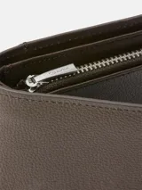 Billetera plegable de piel granulada color marrón oscuro, con logo Calvin Klein grabado en la parte frontal.