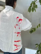 Camisa blanca de lino con cuello de volado y botones personalizados en los puños. Estampado con letras rojas en la espalda.