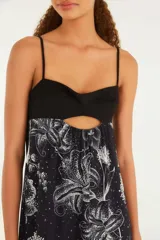 Vestido largo con estampado floral blanco sobre fondo negro, con breteles finos y escote recto. Presenta un corte en la zona del busto con abertura central.