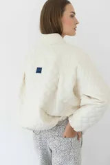 Campera acolchada color crudo con patrón de rombos, cuello alto y cierre frontal.