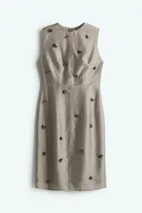 Vestido tubo color gris con cuello redondo y sin mangas. Presenta detalles decorativos de lentejuelas y cuentas brillantes.