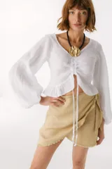 Top blanco de lino italiano con escote en V, mangas largas estilo globo y jareta ajustable en la parte delantera que crea un efecto fruncido y volado en el ruedo.