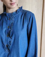 Camisa a rayas verticales color beige y blanco, de corte holgado, con cuello con volados, cierre parcial con botones y mangas largas con puños abotonados.