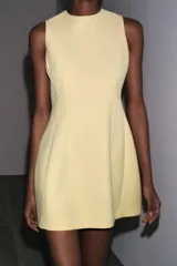 Vestido corto color amarillo pastel, de cuello redondo y sin mangas. Presenta pliegues con volumen en el ruedo y cierre trasero con cremallera oculta.