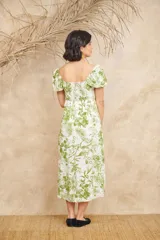 Vestido midi blanco con estampado floral en tonos verdes, escote en V, mangas cortas abullonadas y corte evasé con abertura lateral.