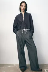 Pantalón ancho gris con textura de espiga, tiro alto, doble cintura elástica ajustable con cordón, pinzas frontales, bolsillos delanteros y falso bolsillo de vivo en la espalda.