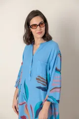 Vestido largo de lino color verde militar con estampado de hojas en tonos azul, naranja y marrón. Tiene cuello mao con botones, mangas tres cuartos y un bolsillo en el pecho.