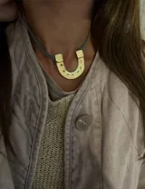 Collar con dije de herradura dorada y cordón celeste.