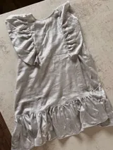 Vestido corto plateado de lino metalizado, con mangas cortas con volados y falda con volados en el ruedo.