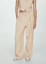 Pantalón color beige de corte wide leg, tiro medio, con trabillas, cierre frontal con botón, gancho y cremallera, detalle de pinzas y diseño largo.