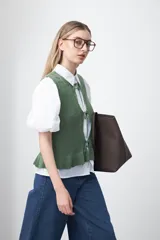 Chaleco tejido color verde musgo, con trama texturada, cuello a la base y cierre frontal con lazos. Presenta un ruedo con volado.