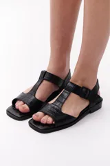 Sandalias negras de cuero con diseño de tiras en forma de T y hebilla lateral.