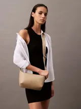 Cartera de hombro Calvin Klein color beige, confeccionada en cuero sintético granulado. Presenta correa ajustable con jacquard con logo, cierre de cremallera en la parte superior, bolsillo interior con ranura para tarjetas y monograma distintivo grabado en la parte delantera.