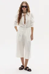 Bermuda de lino color blanco, de corte ancho y largo a la rodilla, con pinzas en la cintura y bolsillos laterales.