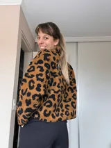Sweater de peluche con cierre de media cremallera, mitad negro liso y mitad con estampado animal print en tonos marrones y negros.