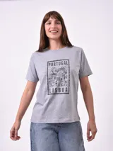 Remera blanca de algodón con cuello redondo y manga corta. Presenta un pequeño bordado en el pecho izquierdo con una figura que parece ser una persona acostada en una tabla de surf o flotador.