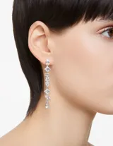 Par de aros largos Swarovski de metal plateado con diseño asimétrico y cristales blancos de diferentes tallas engarzados en cascada.