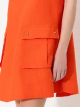 Vestido corto color naranja, sin mangas, con cuello redondo y dos bolsillos frontales con botón.