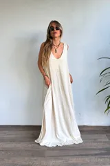 Vestido largo sin mangas, color natural/crudo, con escote en V profundo y corte holgado. Presenta aberturas laterales en la falda.