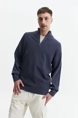 Sweater verde oliva de punto con cuello alto y cierre de medio cierre. Tiene puños y logo bordado en el pecho.