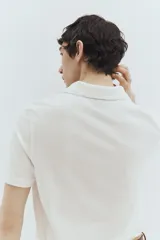 Remera polo blanca de piqué de algodón, corte regular fit, con cuello clásico, tapeta de botones, mangas cortas, remate acanalado en cuello y mangas, y bajo recto con aberturas laterales.