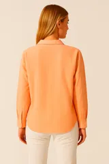 Blusa color beige claro, de corte holgado, con cuello camisero, escote en V y cierre parcial con botones. Presenta mangas largas con puños abotonados y dos bolsillos de parche en el pecho.