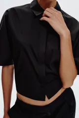 Camisa negra de popelín con cuello solapa y manga ancha por debajo del codo. Detalle de pinzas en la espalda y cierre frontal con botones ocultos por solapa.