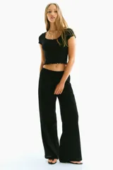 Top corto negro de punto acanalado, de manga corta y ajuste entallado. Presenta ribete de encaje festoneado en el escote redondo y en los bordes de las mangas.