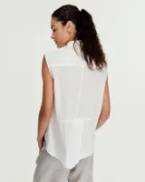 Camisa blanca sin mangas confeccionada en voile de algodón liviano. Tiene cuello camisero, cartera con botones de nácar, bolsillo plaqué en el delantero, costura en centro espalda y recorte en cintura trasera con tajo que se superpone. El ruedo es escalonado, más corto adelante.