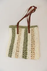 Bolso tipo shopper de rafia color crudo con rayas verticales verdes y beige. Tiene doble asa de cuero marrón.