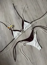 Conjunto de bikini rojo con corpiño triangular con tirantes finos y detalle de aro metálico con forma de corazón en el centro. La bombacha es tipo colaless con tiras finas ajustables en los laterales con detalle de aros metálicos.