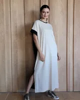 Vestido largo color crudo con cuello redondo y mangas cortas con ribete negro. Tiene corte recto y aberturas laterales en el ruedo.