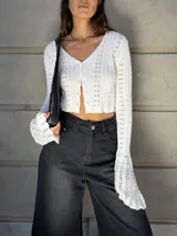 Saco corto de tejido de punto color blanco, con mangas largas y anchas con volados en los puños, y cierre frontal con botones.