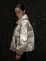 Campera puffer metalizada color plateado, con cuello alto, cierre frontal con cremallera y bolsillos laterales con cierre.