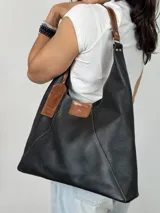 Bolso negro de cuero genuino, tipo tote bag, con doble asa de cuero marrón y etiqueta de cuero con el logo de la marca.