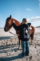 Buzo hoodie negro con capucha y cordón ajustable. Estampado en la espalda con un diseño de palmera dentro de un marco a cuadros.