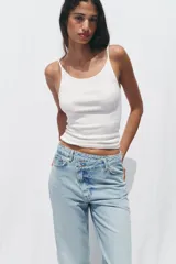 Pantalón de jean celeste de tiro alto, corte recto y largo hasta el tobillo con dobladillo. Tiene cinco bolsillos y cierre frontal cruzado con cremallera y botón.