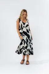 Vestido largo con estampado abstracto en blanco y negro, breteles finos regulables con moños, corte evasé con volado en el ruedo y escote en “V” tanto en el frente como en la espalda.